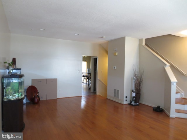 unfurnished living room featuring stairs, wood finished floors, visible vents, and baseboards