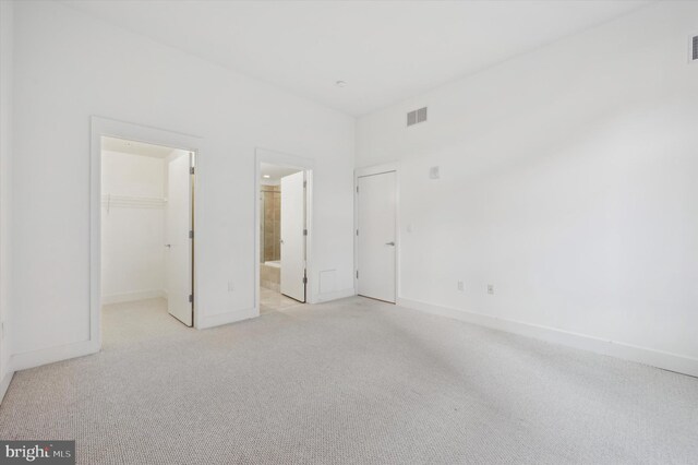 unfurnished bedroom with a walk in closet, light colored carpet, ensuite bath, and a closet