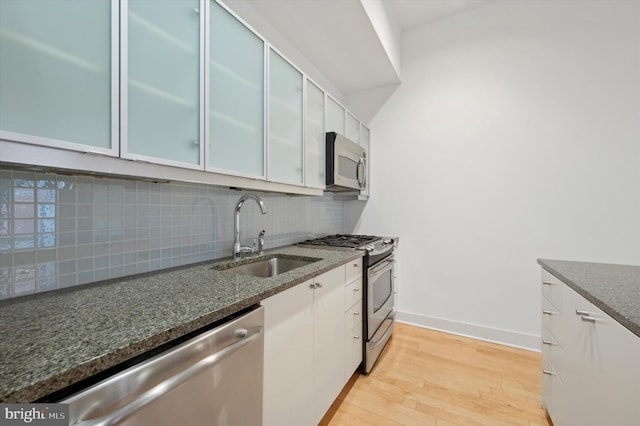 kitchen with appliances with stainless steel finishes, white cabinetry, sink, backsplash, and light hardwood / wood-style flooring