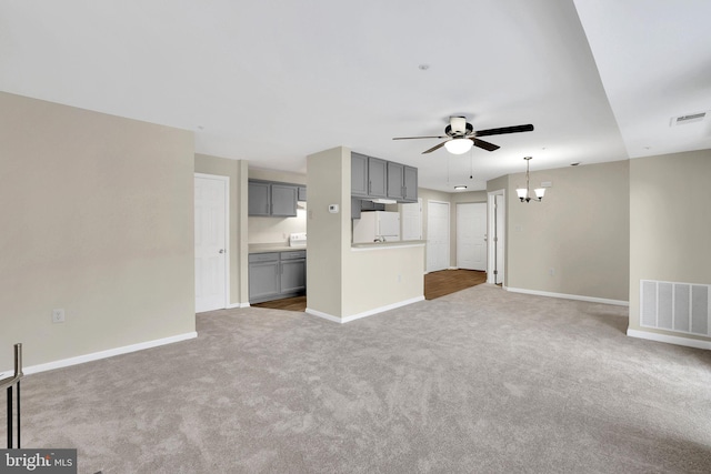 unfurnished living room with ceiling fan with notable chandelier and light carpet