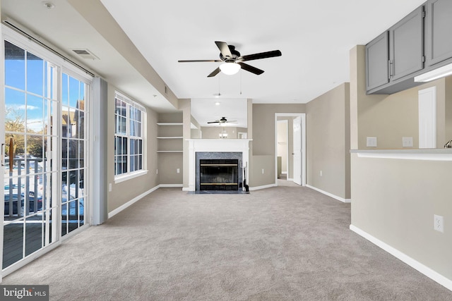 unfurnished living room with built in shelves, light colored carpet, and ceiling fan