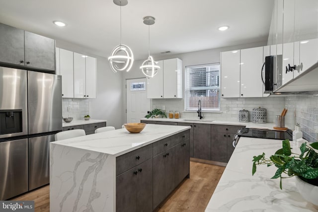 kitchen with sink, white cabinets, hanging light fixtures, a center island, and stainless steel fridge with ice dispenser