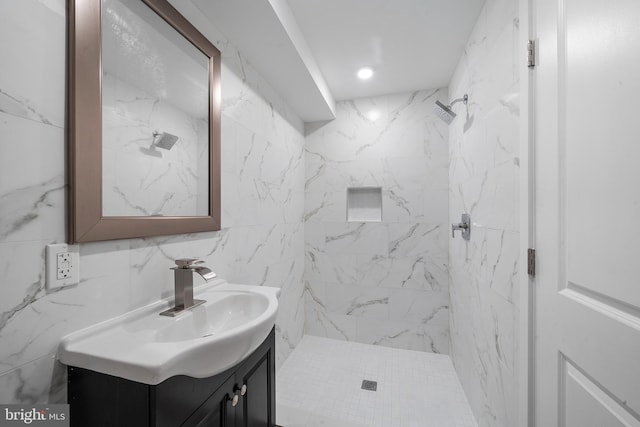 bathroom featuring tiled shower, vanity, and tile walls