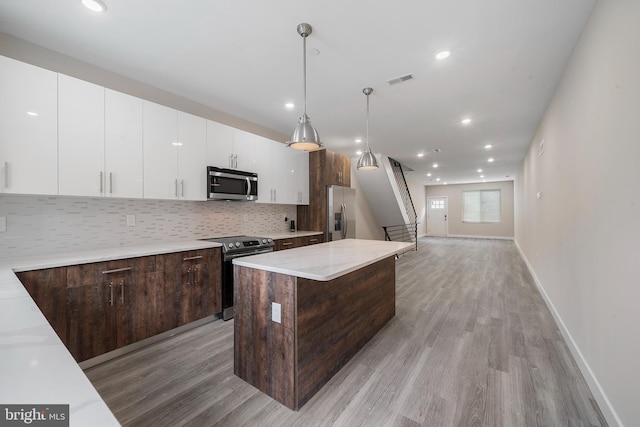 kitchen with a kitchen island, appliances with stainless steel finishes, decorative light fixtures, light stone countertops, and dark brown cabinets