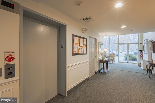 corridor with expansive windows, elevator, and dark colored carpet