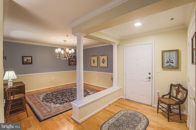 entryway featuring ornate columns, ornamental molding, hardwood / wood-style floors, and a chandelier