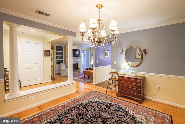 interior space with light hardwood / wood-style flooring, ornamental molding, a chandelier, and ornate columns