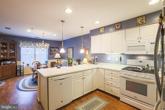 kitchen featuring sink, dark hardwood / wood-style floors, kitchen peninsula, pendant lighting, and white appliances