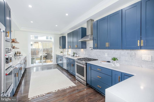 kitchen with stainless steel appliances, wall chimney range hood, decorative backsplash, and blue cabinets