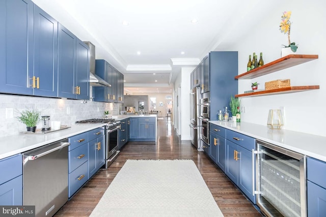 kitchen with stainless steel appliances, wall chimney range hood, blue cabinets, and wine cooler