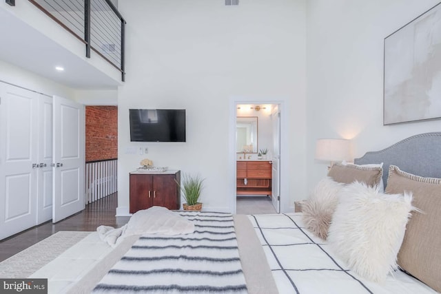 bedroom with hardwood / wood-style flooring, a towering ceiling, ensuite bath, and a closet