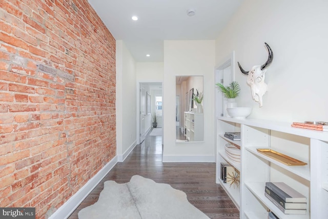 hallway featuring dark wood-type flooring and brick wall