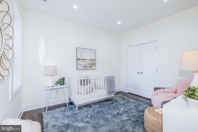 bedroom with dark hardwood / wood-style floors, a closet, and a crib