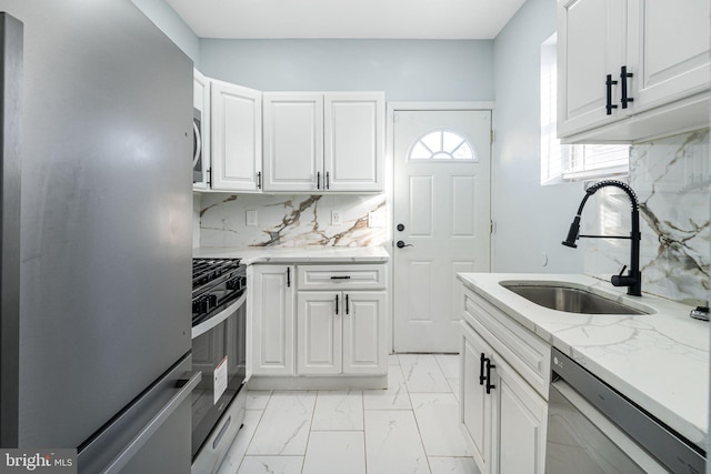 kitchen featuring sink, appliances with stainless steel finishes, white cabinetry, light stone counters, and tasteful backsplash