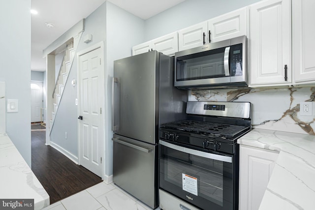 kitchen with decorative backsplash, light stone countertops, white cabinets, and appliances with stainless steel finishes