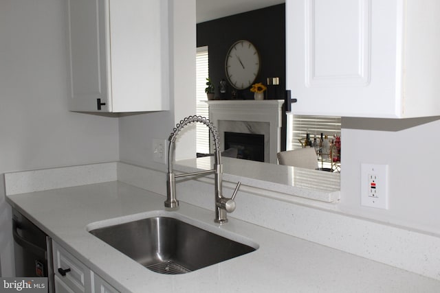 kitchen with sink, a premium fireplace, white cabinetry, black dishwasher, and light stone counters