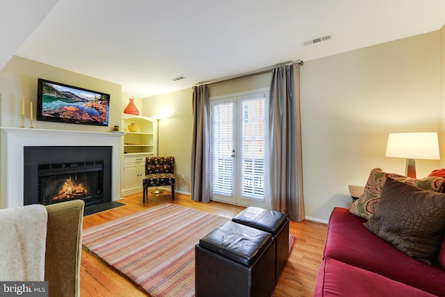 living room with wood-type flooring, built in features, and french doors