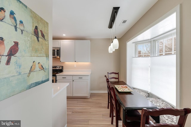 kitchen featuring white cabinetry, decorative light fixtures, light hardwood / wood-style floors, and appliances with stainless steel finishes