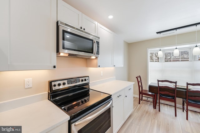 kitchen featuring decorative light fixtures, stainless steel appliances, white cabinets, and light wood-type flooring