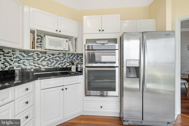 kitchen with stainless steel appliances, white cabinets, backsplash, and dark stone counters