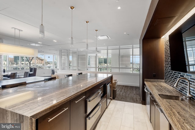 kitchen featuring a spacious island, decorative light fixtures, light stone countertops, and sink