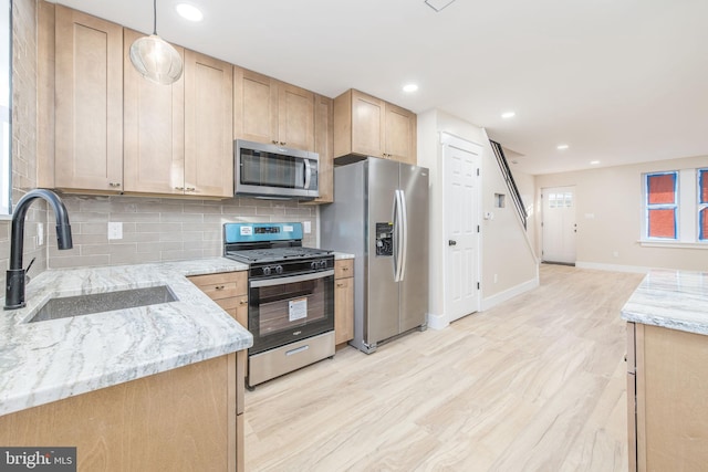 kitchen with appliances with stainless steel finishes, sink, hanging light fixtures, light stone countertops, and light brown cabinets