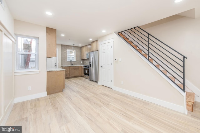 kitchen with stainless steel appliances, tasteful backsplash, sink, and light wood-type flooring