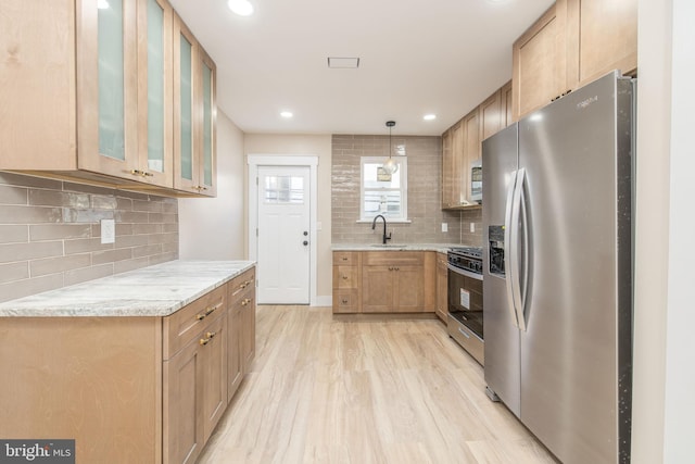 kitchen featuring decorative light fixtures, tasteful backsplash, light hardwood / wood-style floors, stainless steel appliances, and light stone countertops