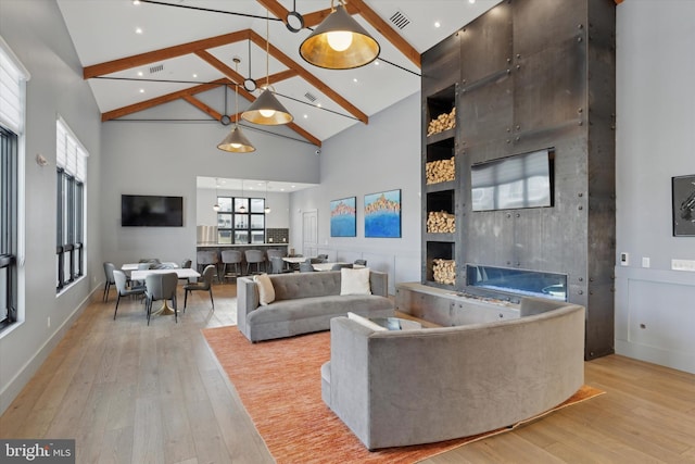 living room featuring light wood-type flooring, high vaulted ceiling, beam ceiling, and a fireplace