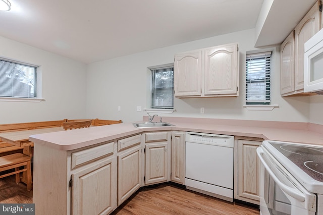 kitchen with white appliances, kitchen peninsula, sink, and light wood-type flooring