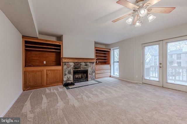 unfurnished living room with ceiling fan, light colored carpet, a stone fireplace, and a wealth of natural light