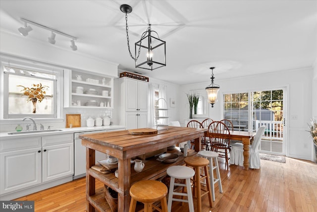 dining space with crown molding, an inviting chandelier, sink, and light wood-type flooring