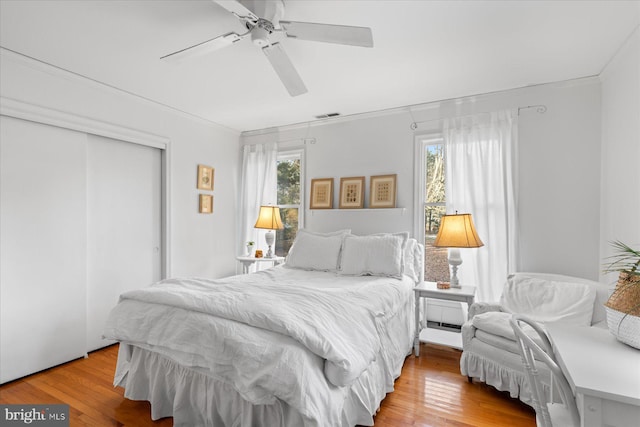 bedroom featuring hardwood / wood-style flooring, crown molding, ceiling fan, and a closet