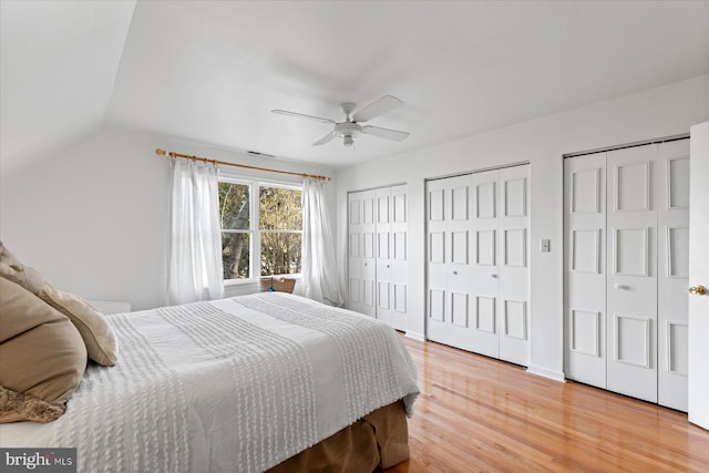 bedroom featuring wood-type flooring, lofted ceiling, two closets, and ceiling fan