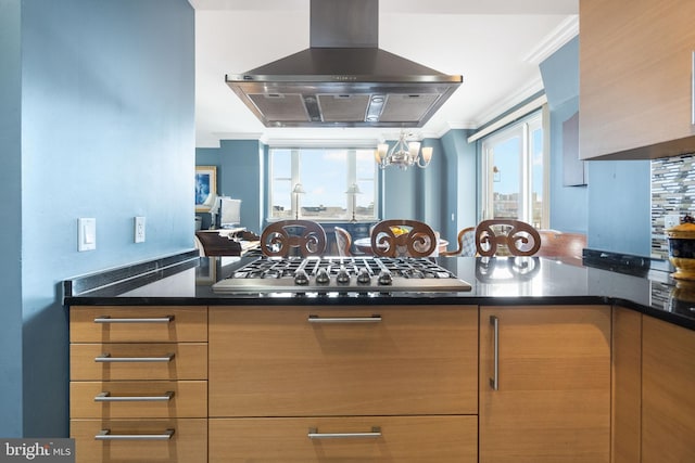 kitchen with dark stone countertops, ornamental molding, stainless steel gas stovetop, and island exhaust hood