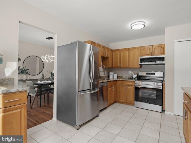 kitchen featuring sink, light stone counters, light tile patterned floors, pendant lighting, and stainless steel appliances