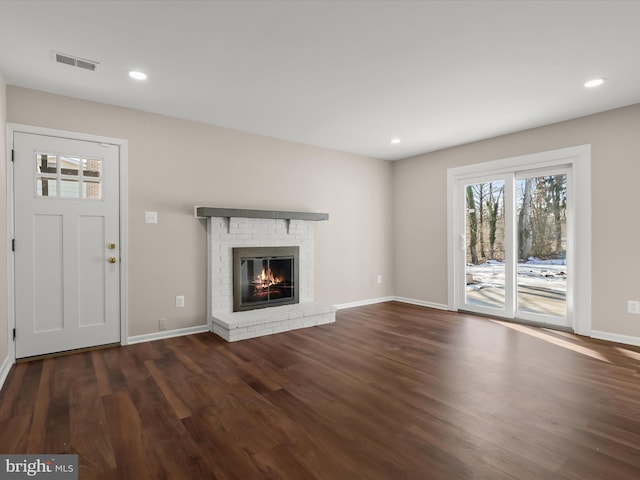 unfurnished living room featuring a brick fireplace and dark wood-type flooring