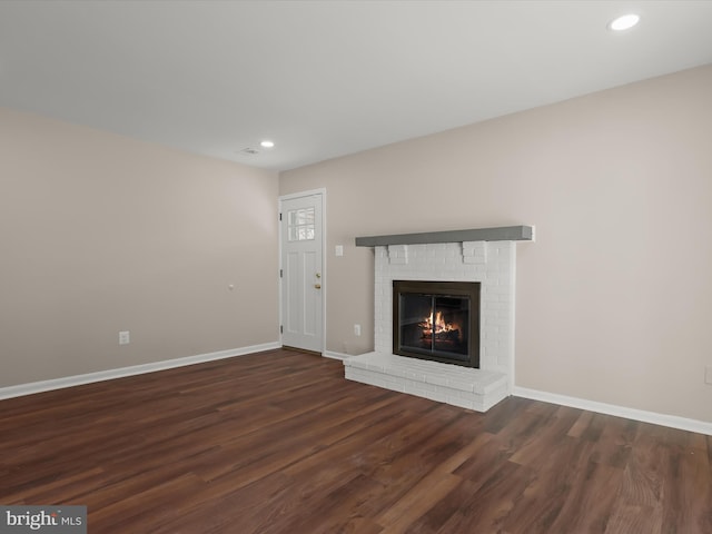 unfurnished living room featuring dark hardwood / wood-style flooring and a brick fireplace