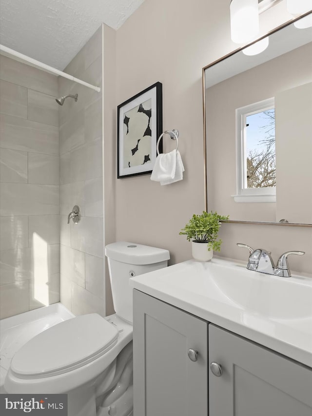 bathroom with vanity, a tile shower, a textured ceiling, and toilet