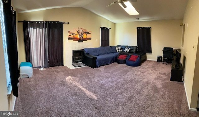 carpeted living room featuring a tiled fireplace, ceiling fan, and vaulted ceiling with skylight