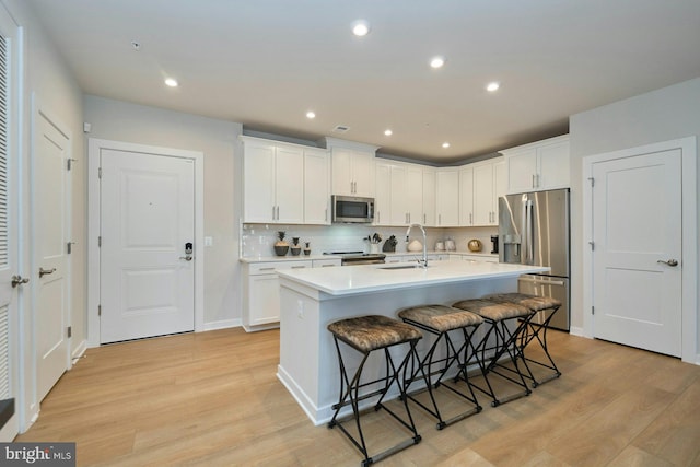 kitchen featuring a kitchen bar, light wood-type flooring, appliances with stainless steel finishes, an island with sink, and white cabinets