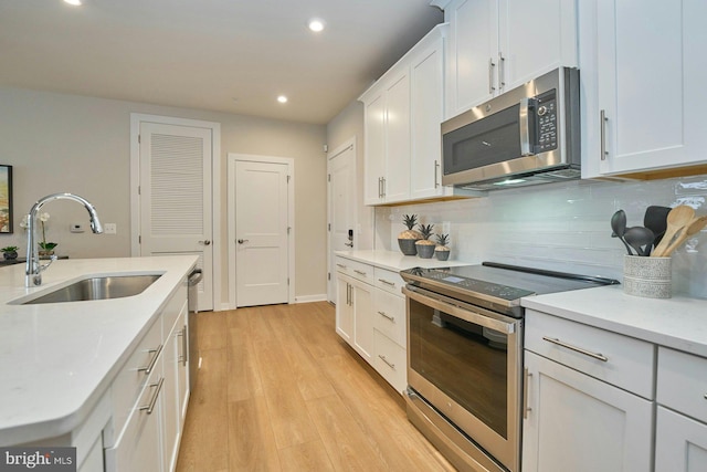 kitchen featuring sink, white cabinetry, backsplash, stainless steel appliances, and light hardwood / wood-style floors