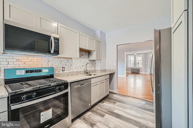 kitchen featuring sink, white cabinets, light hardwood / wood-style floors, stainless steel appliances, and light stone countertops