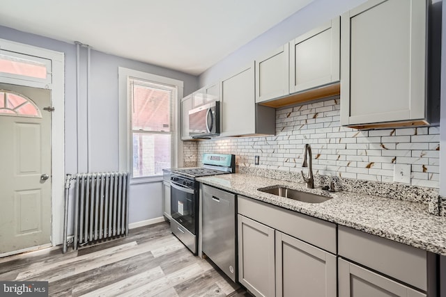 kitchen featuring sink, gray cabinetry, light stone counters, appliances with stainless steel finishes, and radiator heating unit