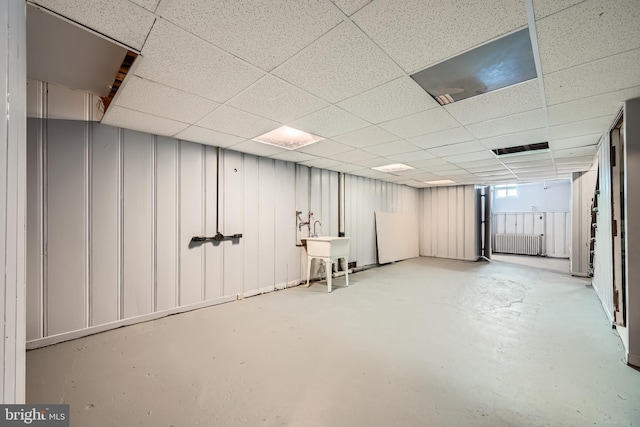 basement with sink, a paneled ceiling, and radiator