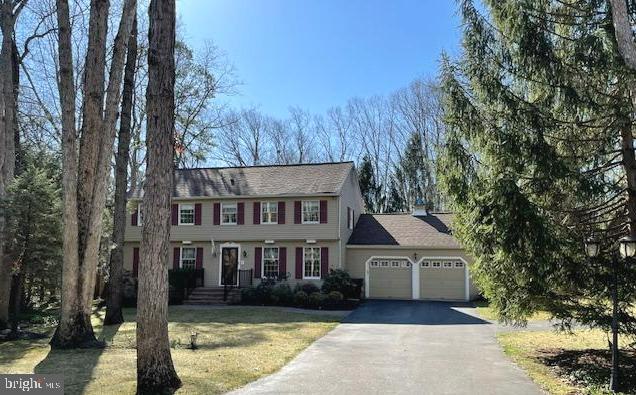 colonial-style house featuring a front lawn, an attached garage, and driveway