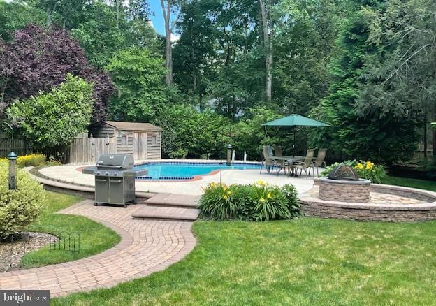 pool with a fire pit, an outbuilding, a grill, a storage unit, and a patio