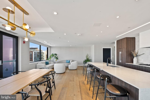 kitchen with an island with sink, sink, light hardwood / wood-style floors, and decorative backsplash