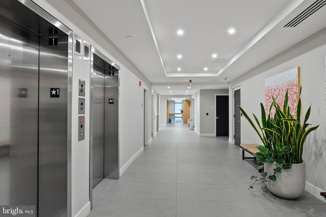 hallway with a tray ceiling, elevator, and light tile patterned flooring