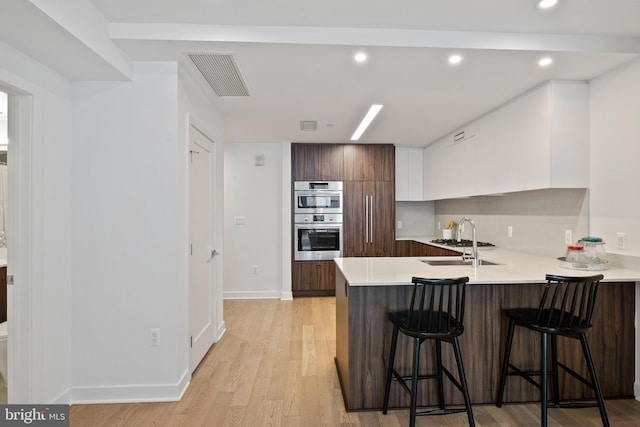 kitchen with sink, white cabinetry, a kitchen breakfast bar, kitchen peninsula, and stainless steel double oven